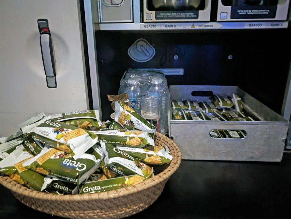 Turkish Airlines Food Review Economy Class 24 A basket filled with packaged Greta snacks sits on a counter next to a metal tray of more snacks and plastic cups, reminiscent of the delicious assortment found in Turkish Airlines meals.