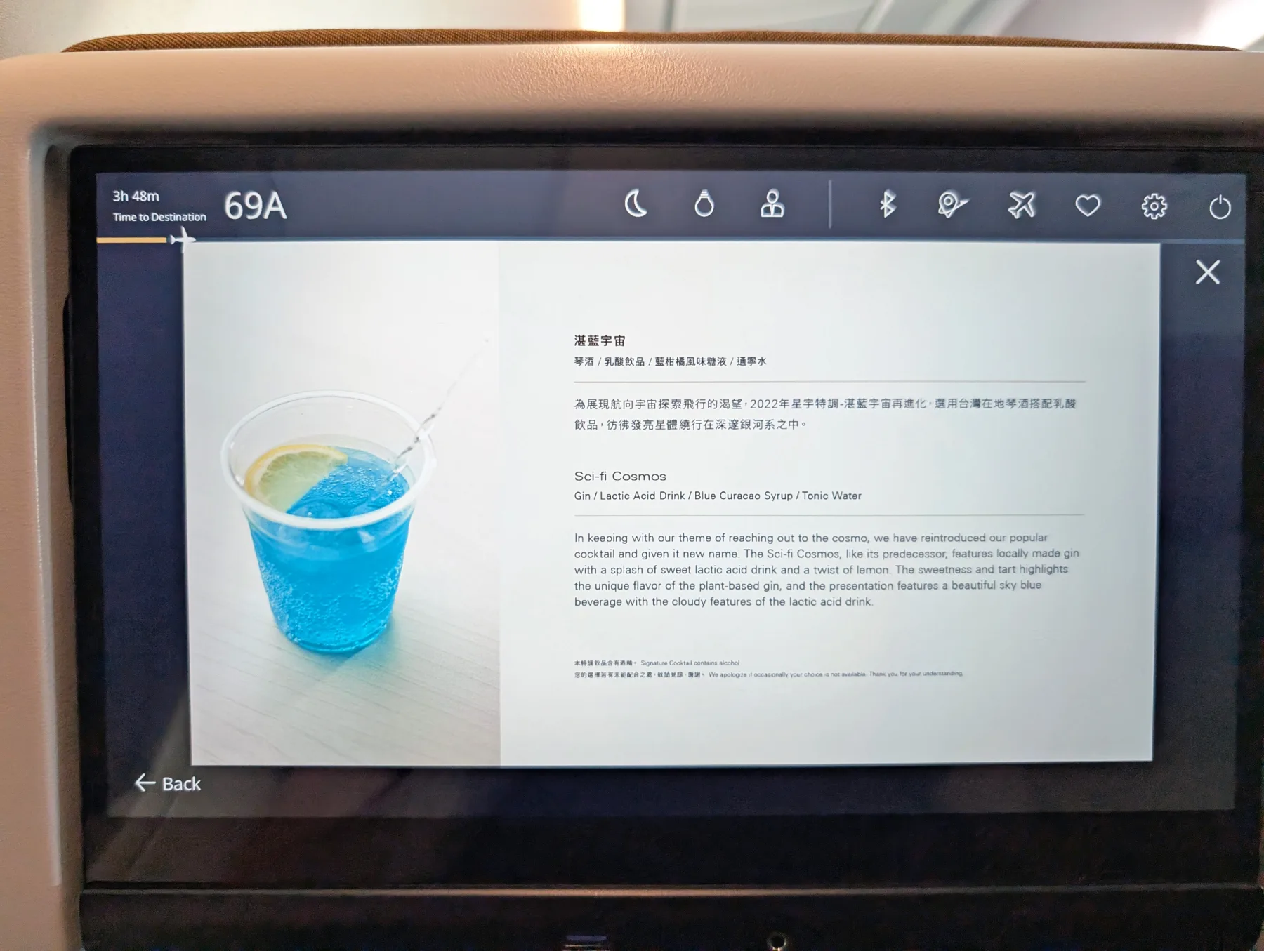 Starlux Airlines Review 2025: Taipei to Singapore 12 A plastic cup with a blue drink and a lemon slice sits on a tray table, shown on an airplane seatback screen displaying a description of the beverage.