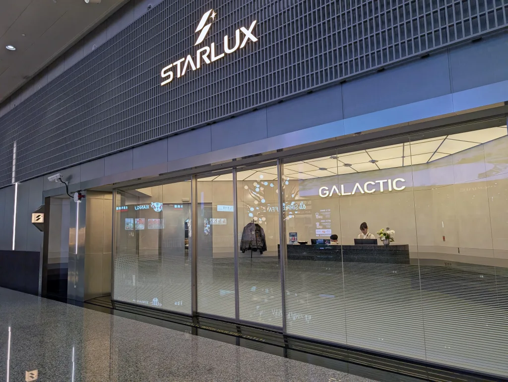 Starlux Airlines Review 2025: Taipei to Singapore 16 Glass entrance to the Starlux Galactic lounge with a reception desk inside and a staff member seated behind it.
